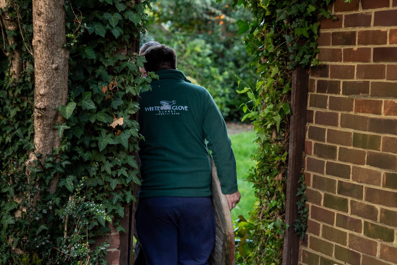 White Glove Surrey mover carrying wrapped furniture through a garden gate